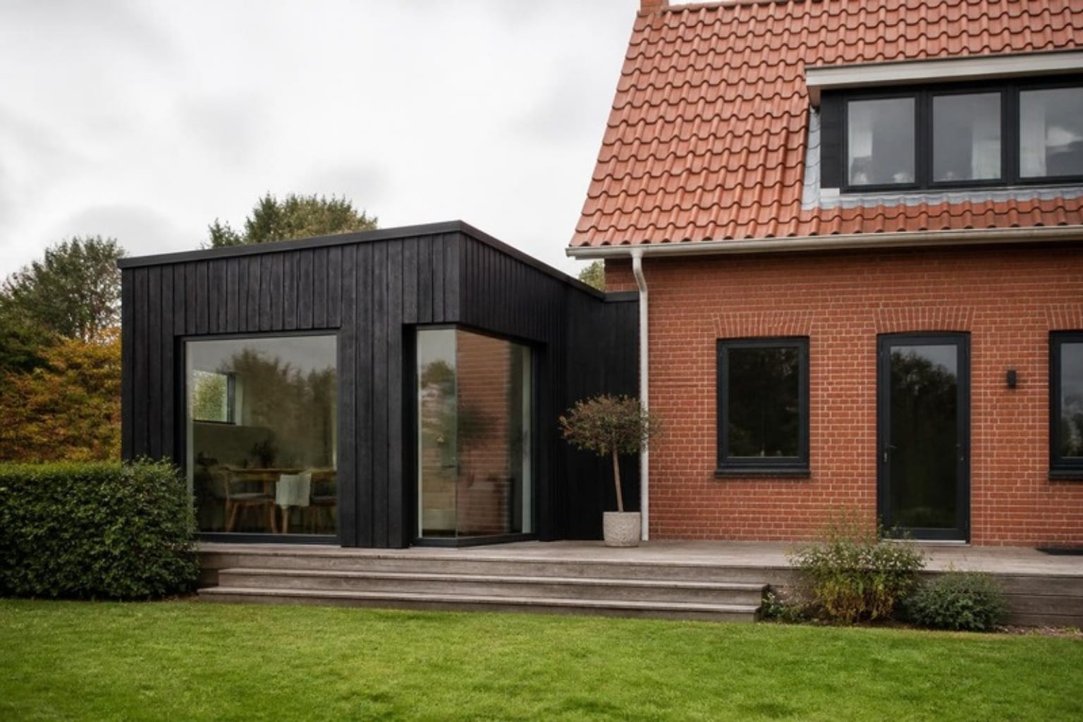 Tilbygning med sort træbeklædning og store vinduer på murstenshus